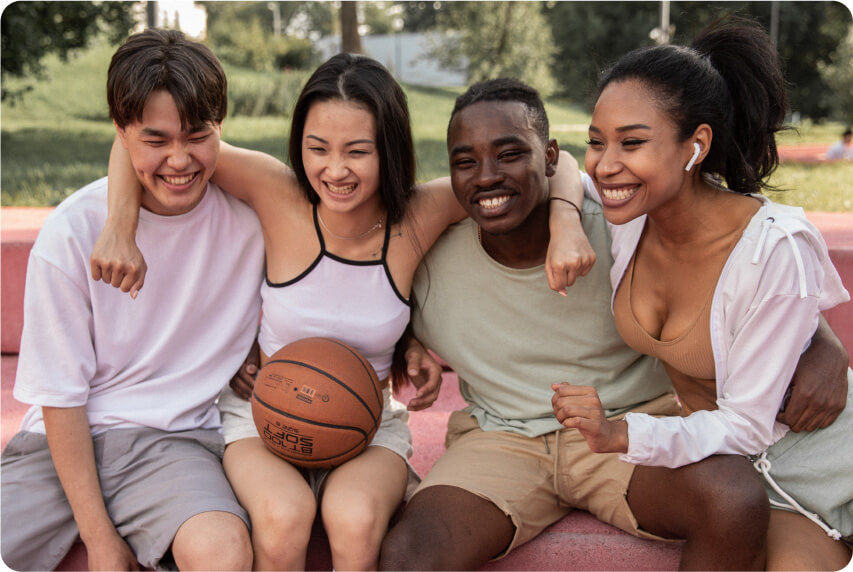 A group of friends sit together with their arms around each other, one of them is holding a basketball